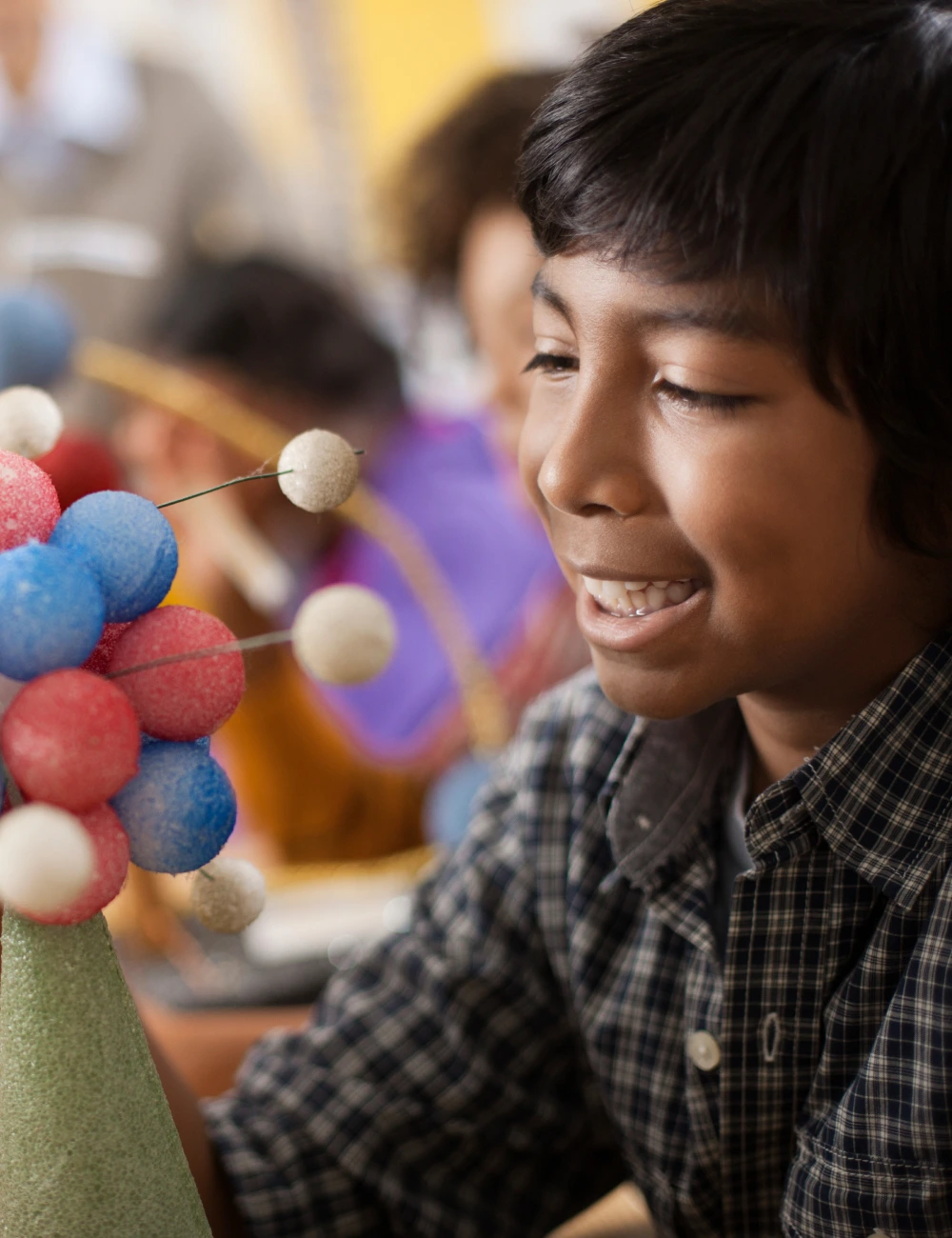 Smiling boy looking at a colorful molecular model in a classroom setting.